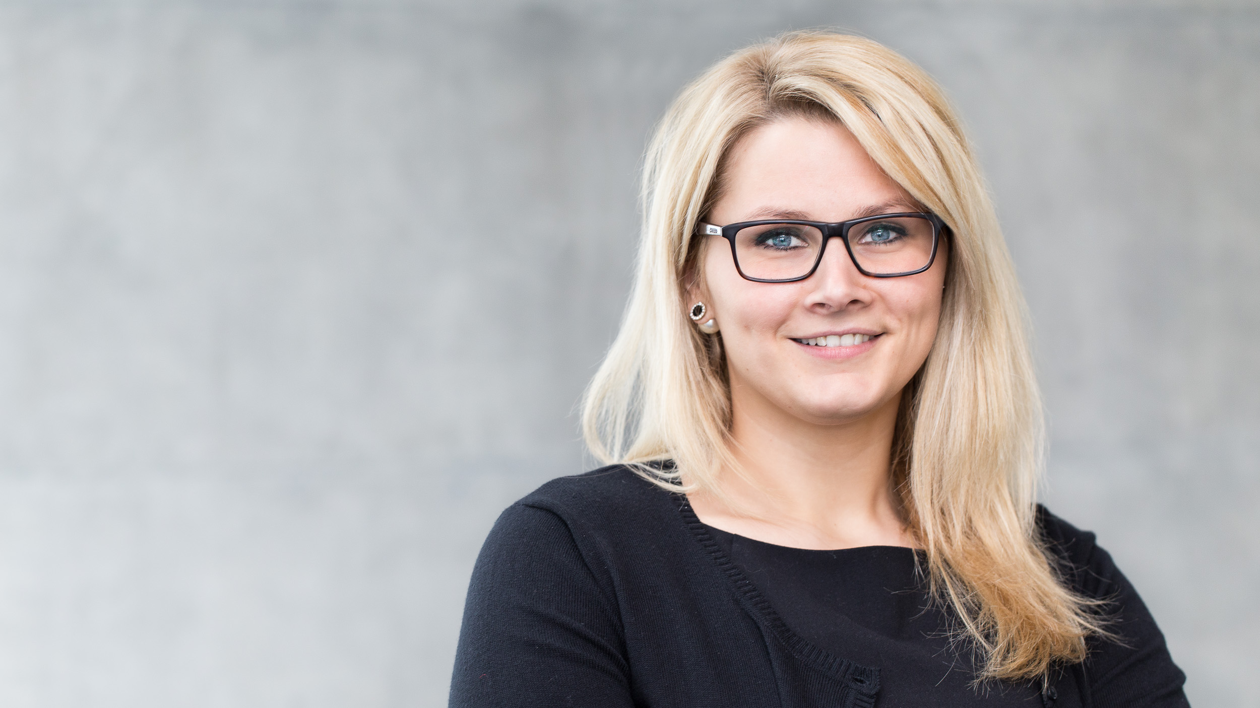 photo-genic: Portraitfotografie – Businessfotografie photo-genic Business Portrait: Frau, schwarz gekleidet mit Brille, vor weißer Wand