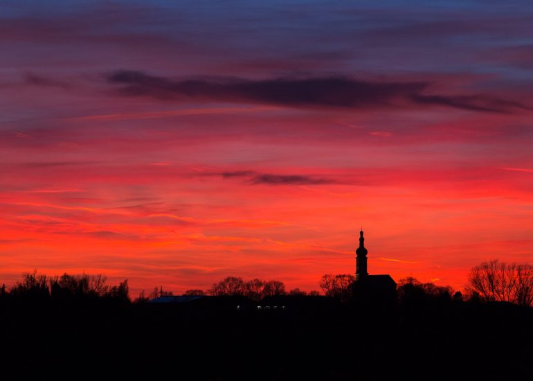 Portfolio Landschaftsfotografie: Tief rot gefärbter Himmel über einer Dorfkirche bei Sonnenuntergang