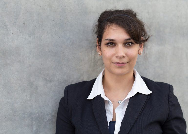 Portfolio -Portraitfotografie - Business Portraits: Junge Geschäftsfrau stehend vor grauer Wand.