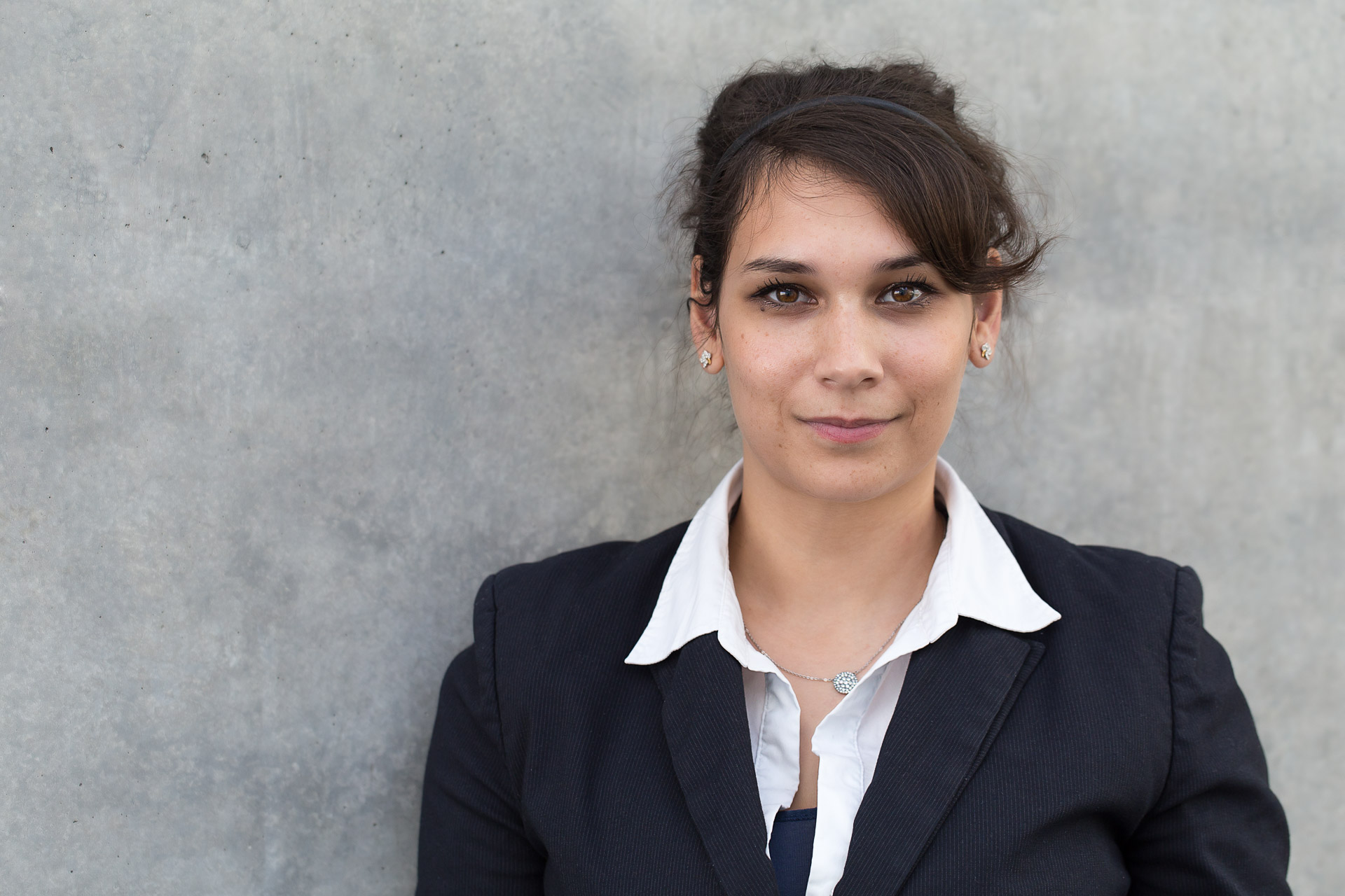 Portfolio -Portraitfotografie - Business Portraits: Junge Geschäftsfrau stehend vor grauer Wand.