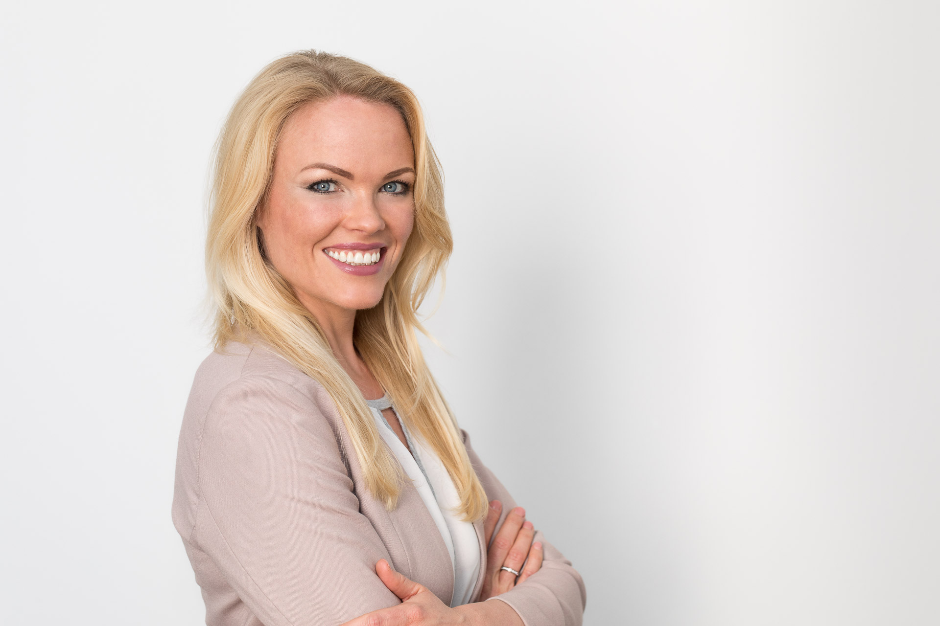 Portraitfotografie - Business Portraits: Lächelnde Geschäftsfrau stehend vor weißer Wand.