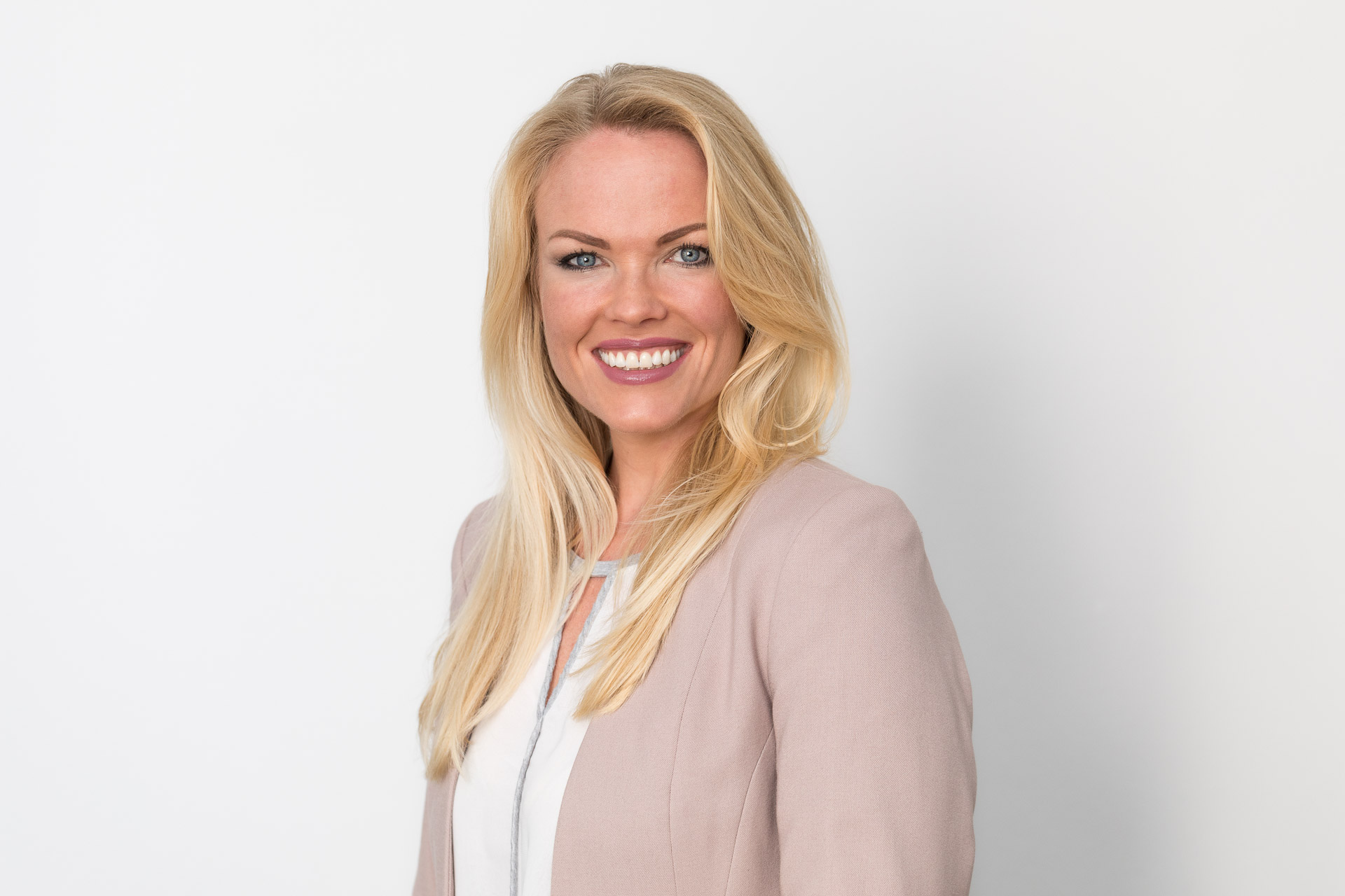 Portraitfotografie - Business Portraits: Lächelnde Geschäftsfrau stehend vor weißer Wand.