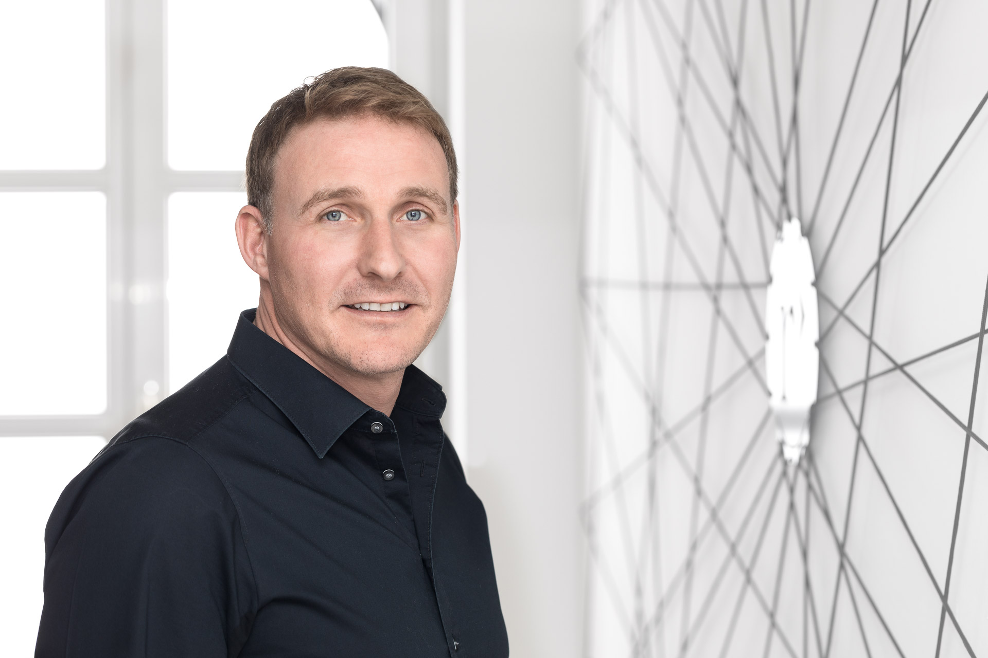 Portraitfotografie und Business Portraits: Mann mittleren Alters stehend vor Fenster und weißer Wand