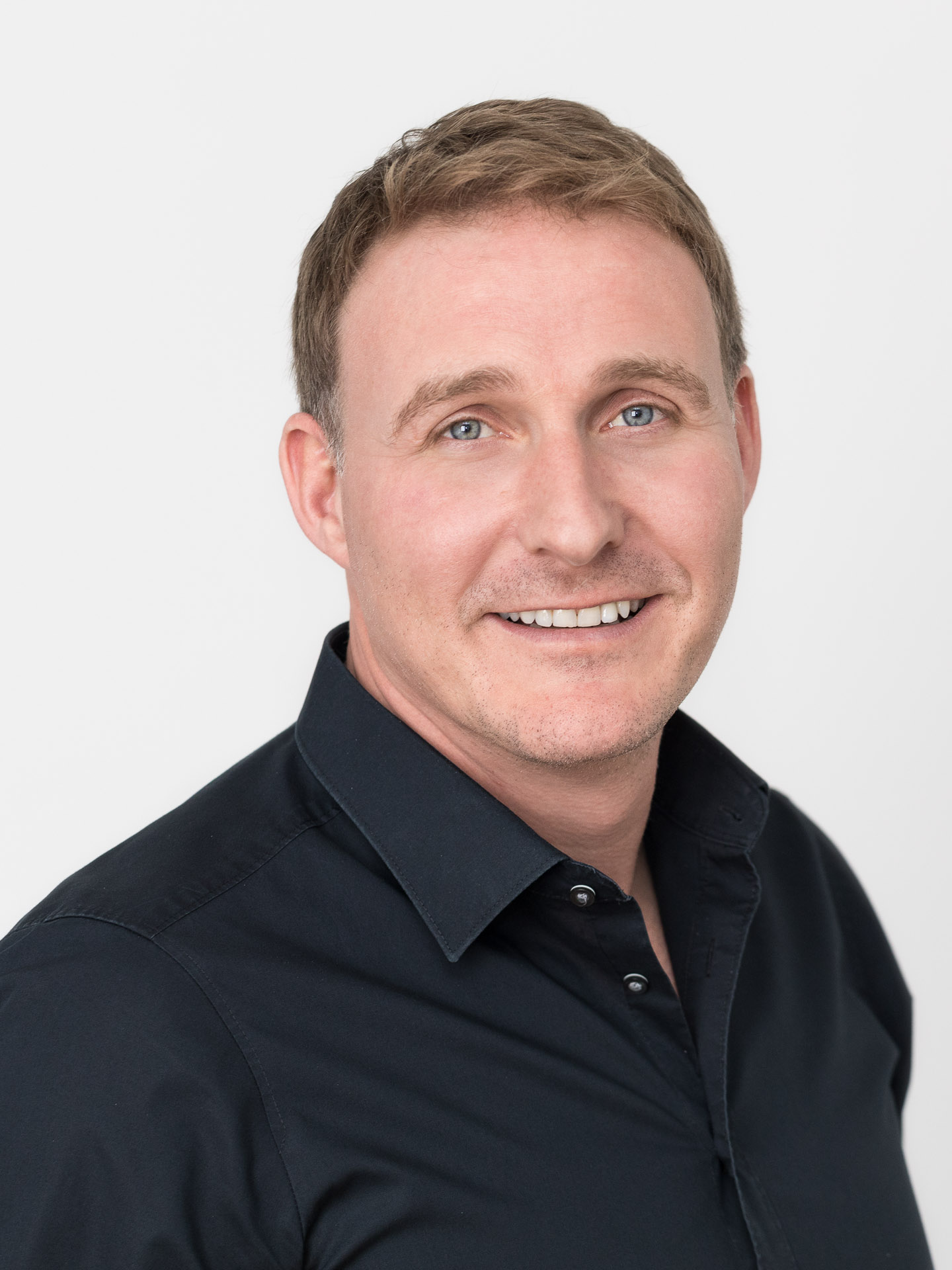 Portraitfotografie und Business Portraits: Mann mittleren Alters stehend vor weißer Wand.