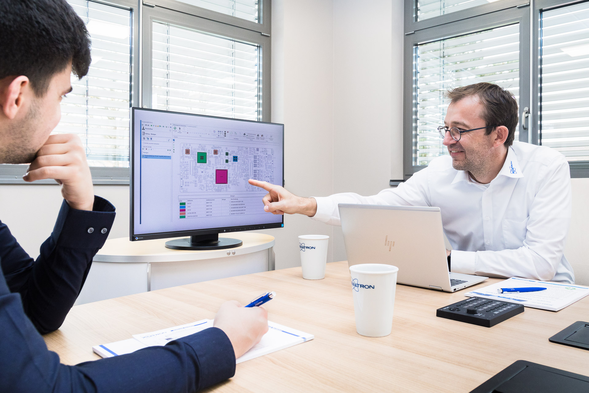 Businessfotografie: Mitarbeiter zeigt auf einen Bildschirm, ein Kollege hört zu