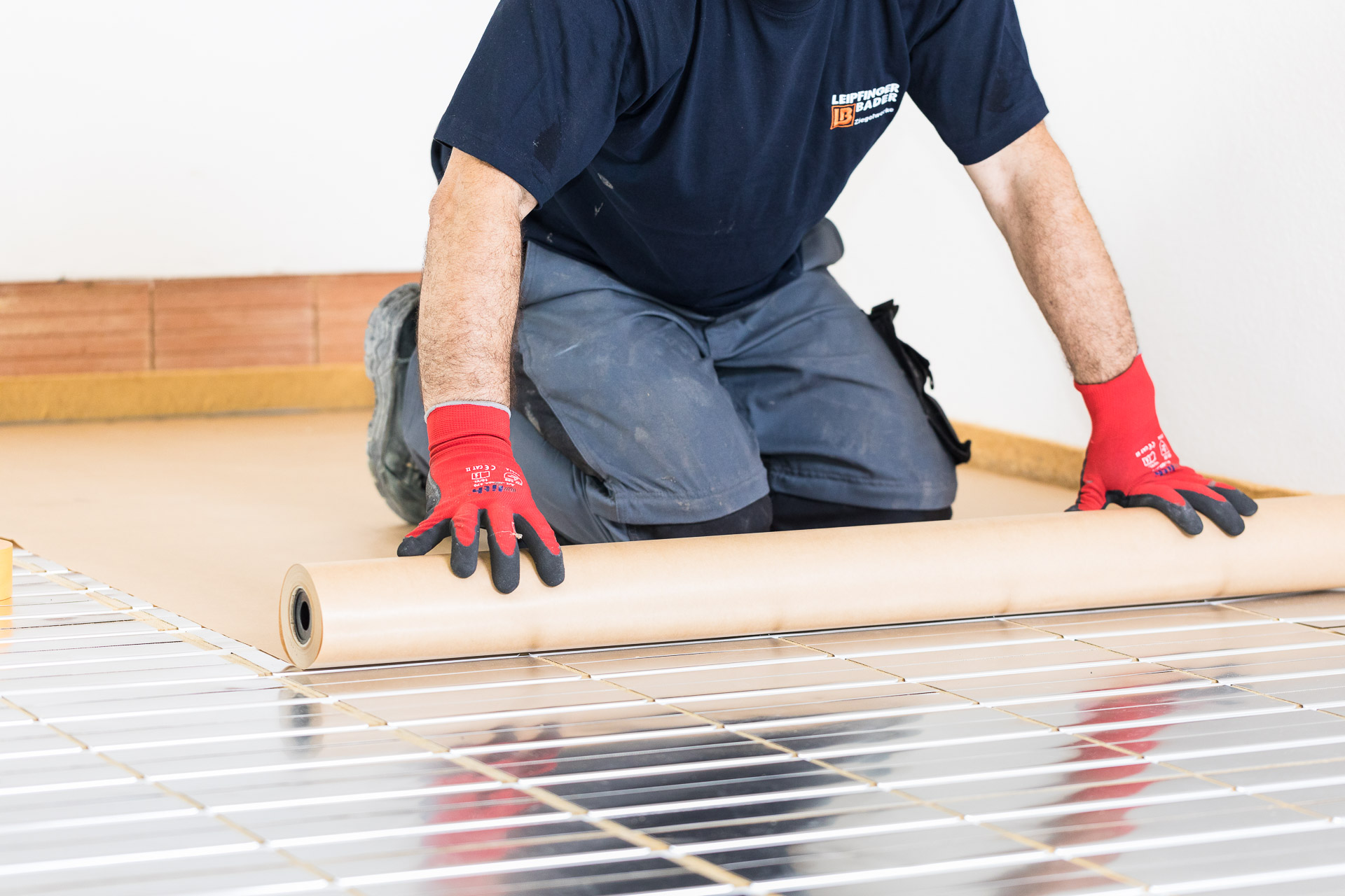 Handwerker rollt Trennschicht über die Elemente der Fußbodenheizung. Indurstriefotografie - Baubranche von photo-genic.