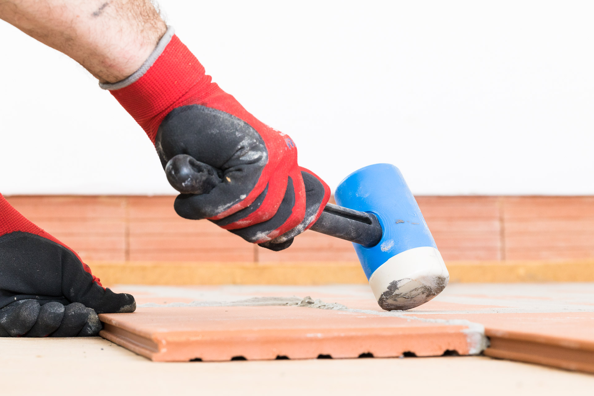 Handwerker verlegt Estrichziegel und klopft mit Hammer auf den Ziegel. Indurstriefotografie - Baubranche von photo-genic.