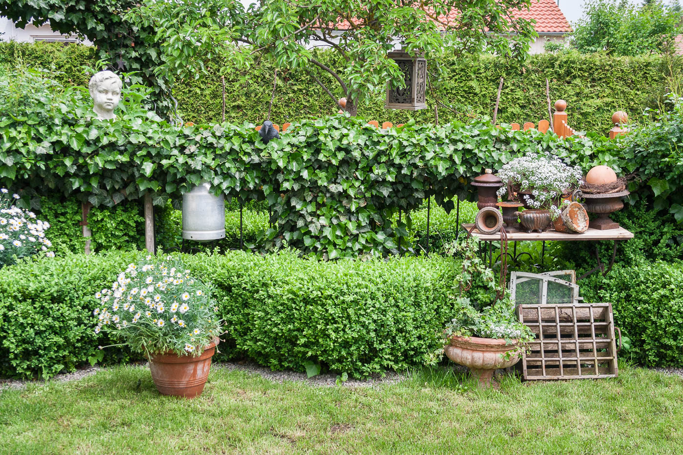 Gartenfotografie - Gartenbilder: Arrangement aus patinierten Ton- und Eisentöpfen, Milchkanne, alte Holzfensterscheiben umgeben von Grün