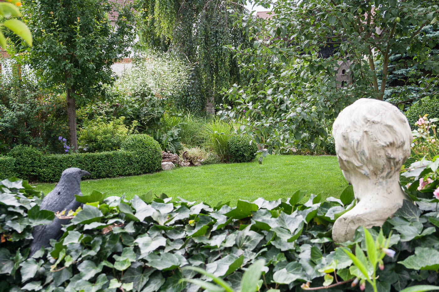 Ein Rabe und "Kindskopf" aus Ton, umrankt von Efeu, wachen über den Garten.